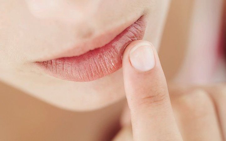 index finger placing glossy products over lips.